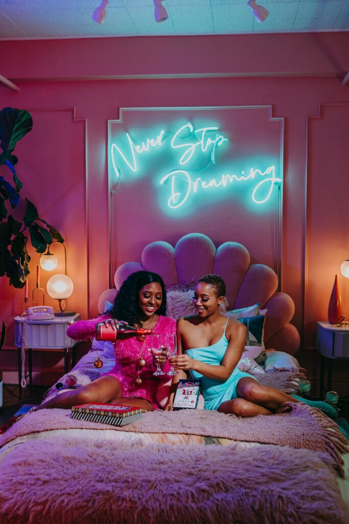 Two friends celebrate in a cozy room with neon lights, embodying warmth and joy.